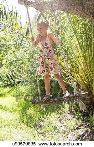Girl standing swinging on tree swing in garden View Large Photo Image Stock Photography - Girl standing swinging on tree swing in garden. Fotosearch