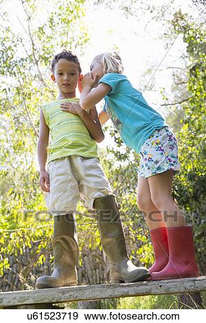Girl whispering to boy whilst standing on garden bench View Large Photo Image Stock Photo - Girl whispering to boy whilst standing on garden bench. Fotosearch