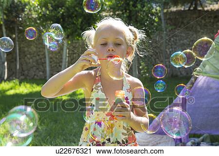 Stock Image - Girls blowing bubbles in summer garden party. Fotosearch
