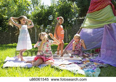 Stock Photography - Girls blowing bubbles in summer garden party. Fotosearch