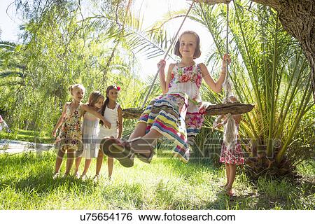 Stock Photograph - Girls queueing for tree swing in garden. Fotosearch