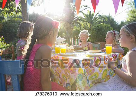 Stock Image - Girls sitting at table with birthday party food. Fotosearch