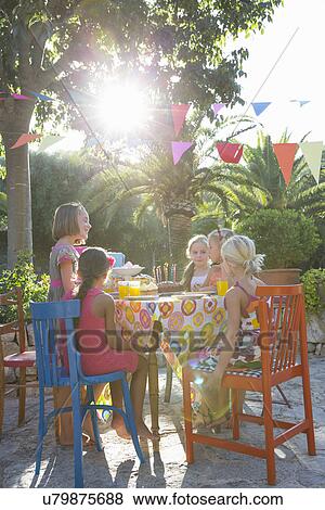 Stock Photo - Girls sitting at table with birthday party food. Fotosearch