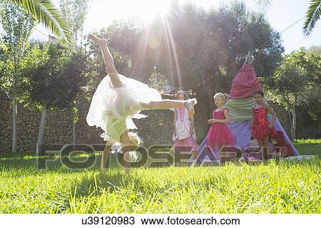 Stock Image - Girls watching friend in fairy costume doing cartwheel in garden. Fotosearch