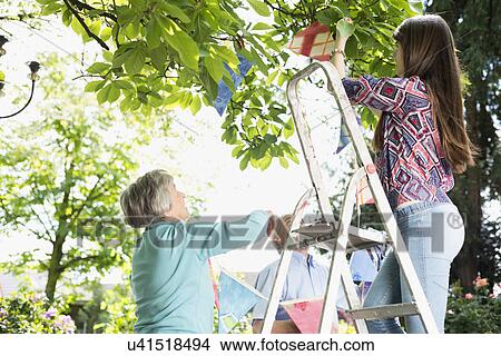 Picture - Grandparents and granddaughter hanging up bunting. Fotosearch
