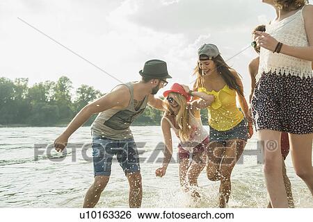 Stock Photograph - Group of young friends running in lake. Fotosearch