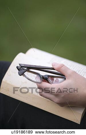 Stock Photo - Hand with eye glasses keeping book open. Fotosearch