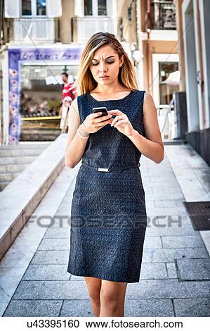 Impatient young woman texting on smartphone on city street View Large Photo Image Stock Image - Impatient young woman texting on smartphone on city street. Fotosearch