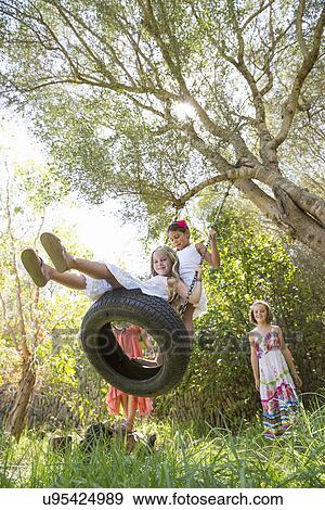 Low angle view of four girls playing on tree tire swing in garden View Large Photo Image Stock Photo - Low angle view of four girls playing on tree tire swing in garden. Fotosearch