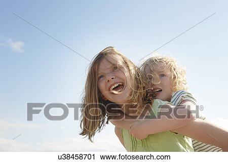 Low angle view of girl giving sister piggy back at coast View Large Photo Image Stock Image - Low angle view of girl giving sister piggy back at coast. Fotosearch