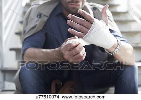 Man bandaging hand on staircase View Large Photo Image Picture - Man bandaging hand on staircase. Fotosearch