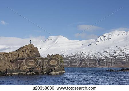 Stock Photograph - Man standing on edge of islet, Iceland. Fotosearch