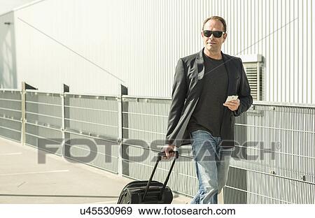Mature man pulling wheeled suitcase View Large Photo Image Stock Photo - Mature man pulling wheeled suitcase. Fotosearch