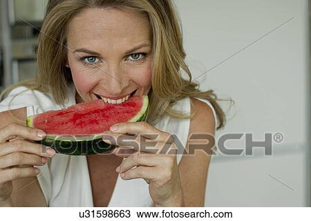 Stock Image - Mature woman biting watermelon. Fotosearch