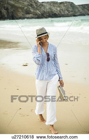 Mature woman chatting on smartphone whilst strolling on beach, Camaret-sur-mer, Brittany, France View Large Photo Image Stock Photo - Mature woman chatting on smartphone whilst strolling on beach, Camaret-sur-mer, Brittany, France. Fotosearch