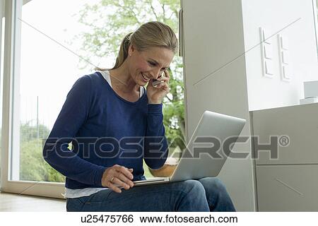Stock Photograph - Mature woman using laptop on cell phone. Fotosearch