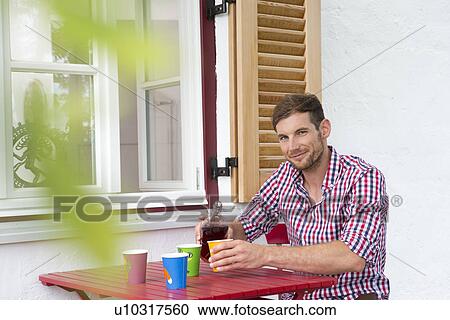 Stock Image - Mid adult man at table pouring soft drink. Fotosearch