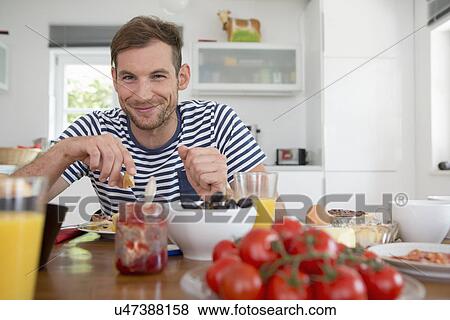 Mid adult man eating at kitchen table View Large Photo Image Stock Photo - Mid adult man eating at kitchen table. Fotosearch