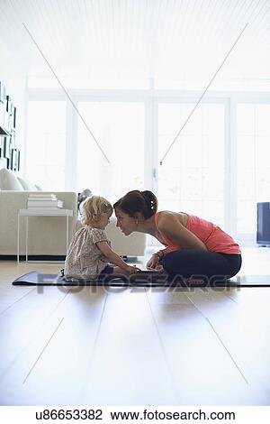 Stock Image - Mid adult mother and toddler daughter practicing lotus position in living room. Fotosearch