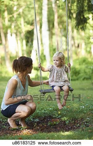 Mid adult mother and toddler daughter playing on garden swing View Large Photo Image Stock Photography - Mid adult mother and toddler daughter playing on garden swing. Fotosearch