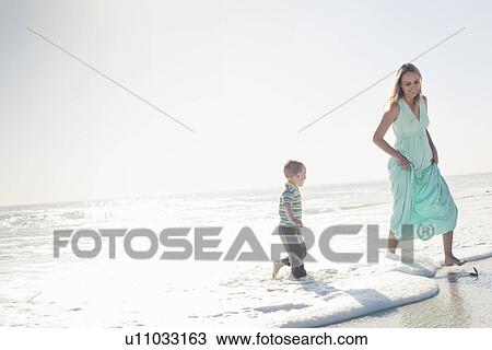 Stock Image - Mid adult mother and young son running away from ocean wave, Cape Town, Western Cape, South Africa. Fotosearch