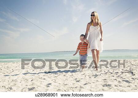 Stock Image - Mid adult mother and young son strolling on beach, Cape Town, Western Cape, South Africa. Fotosearch
