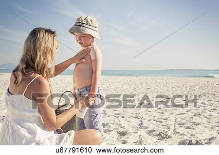 Stock Image - Mid adult mother applying sun lotion to young son on beach, Cape Town, Western Cape, South Africa. Fotosearch
