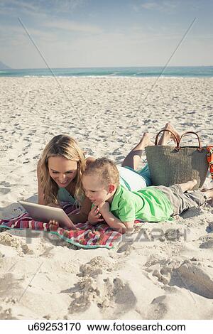 Stock Image - Mid adult mother looking at digital tablet with young son on beach, Cape Town, Western Cape, South Africa. Fotosearch