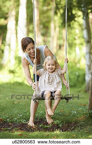 Mid adult mother pushing toddler daughter on garden swing View Large Photo Image Stock Image - Mid adult mother pushing toddler daughter on garden swing. Fotosearch