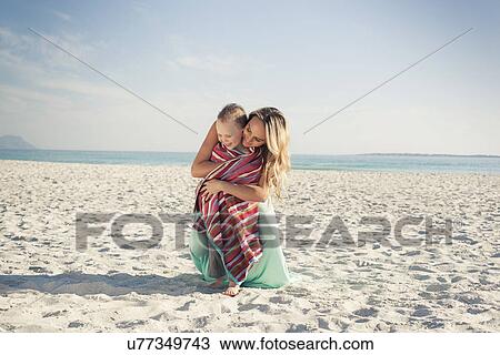 Stock Image - Mid adult mother wrapping son in a towel at beach, Cape Town, Western Cape, South Africa. Fotosearch
