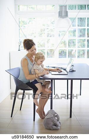 Stock Image - Mid adult woman and toddler daughter typing on laptop. Fotosearch