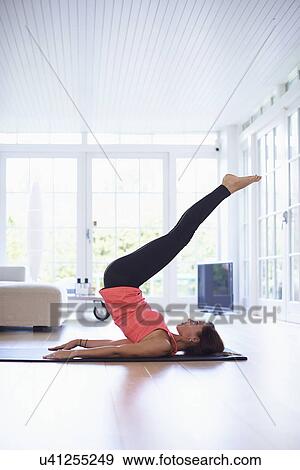 Mid adult woman lying on back practicing yoga in living room View Large Photo Image Stock Photo - Mid adult woman lying on back practicing yoga in living room. Fotosearch