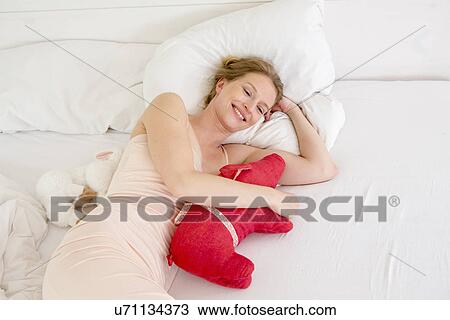 Stock Image - Mid adult woman lying on bed holding soft toy. Fotosearch