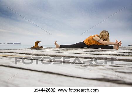 Stock Image - Mid adult woman practicing yoga on wooden sea pier. Fotosearch