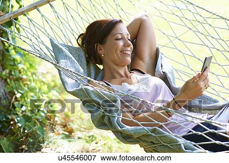 Mid adult woman reclining in garden hammock looking at smartphone View Large Photo Image Stock Photo - Mid adult woman reclining in garden hammock looking at smartphone. Fotosearch