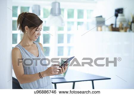 Mid adult woman using digital tablet in dining room View Large Photo Image Stock Photograph - Mid adult woman using digital tablet in dining room. Fotosearch