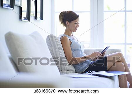 Mid adult woman using digital tablet on living room sofa View Large Photo Image Stock Image - Mid adult woman using digital tablet on living room sofa. Fotosearch