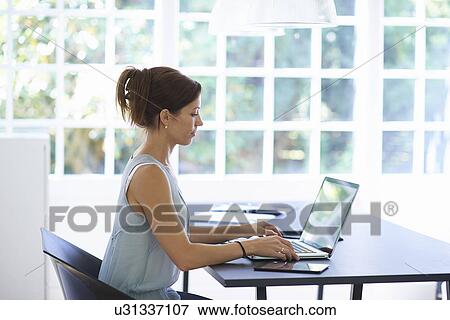 Mid adult woman working on laptop in dining room View Large Photo Image Stock Photo - Mid adult woman working on laptop in dining room. Fotosearch