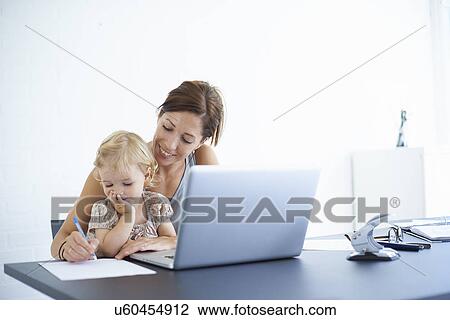 Stock Image - Mid adult woman writing notes with toddler daughter on her lap. Fotosearch