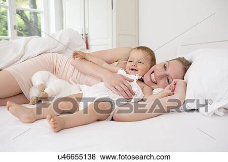 Mother and baby daughter lying on bed View Large Photo Image Stock Photo - Mother and baby daughter lying on bed. Fotosearch