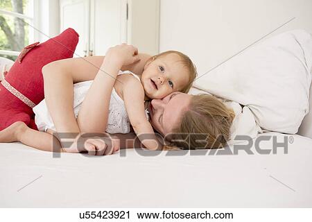 Stock Image - Mother hugging baby daughter on bed. Fotosearch