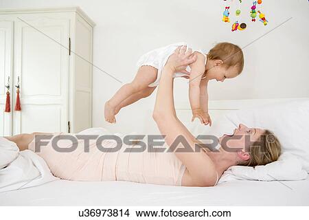 Mother lifting baby daughter on bed View Large Photo Image Picture - Mother lifting baby daughter on bed. Fotosearch