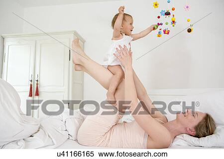 Mother lifting baby daughter on bed View Large Photo Image Stock Photography - Mother lifting baby daughter on bed. Fotosearch