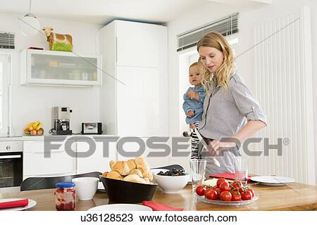 Mother setting kitchen table while holding baby daughter View Large Photo Image Stock Image - Mother setting kitchen table while holding baby daughter. Fotosearch