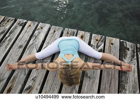 Overhead view of mid adult woman with arms and legs outstretched practicing yoga on wooden sea pier View Large Photo Image Stock Photo - Overhead view of mid adult woman with arms and legs outstretched practicing yoga on wooden sea pier. Fotosearch