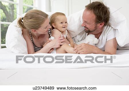 Stock Photo - Parents playing with baby daughter under duvet. Fotosearch