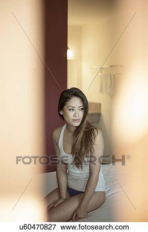 Stock Photo - Partially dressed woman sitting on bed. Fotosearch
