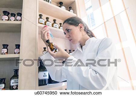 Stock Image - Pharmacist in pharmacy, examining test tube contents. Fotosearch