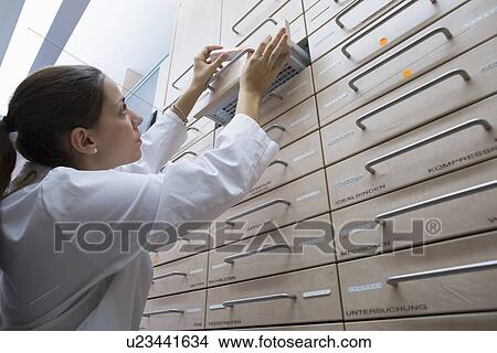 Pharmacist in pharmacy filing medicine away in drawer View Large Photo Image Picture - Pharmacist in pharmacy filing medicine away in drawer. Fotosearch