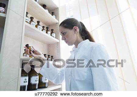 Stock Image - Pharmacist in pharmacy holding medicine bottle. Fotosearch